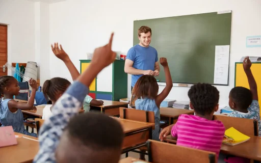 Sala de aula com crianças levantando as mãos para responder o professor. Ambiente educativo com interação entre alunos e professor.