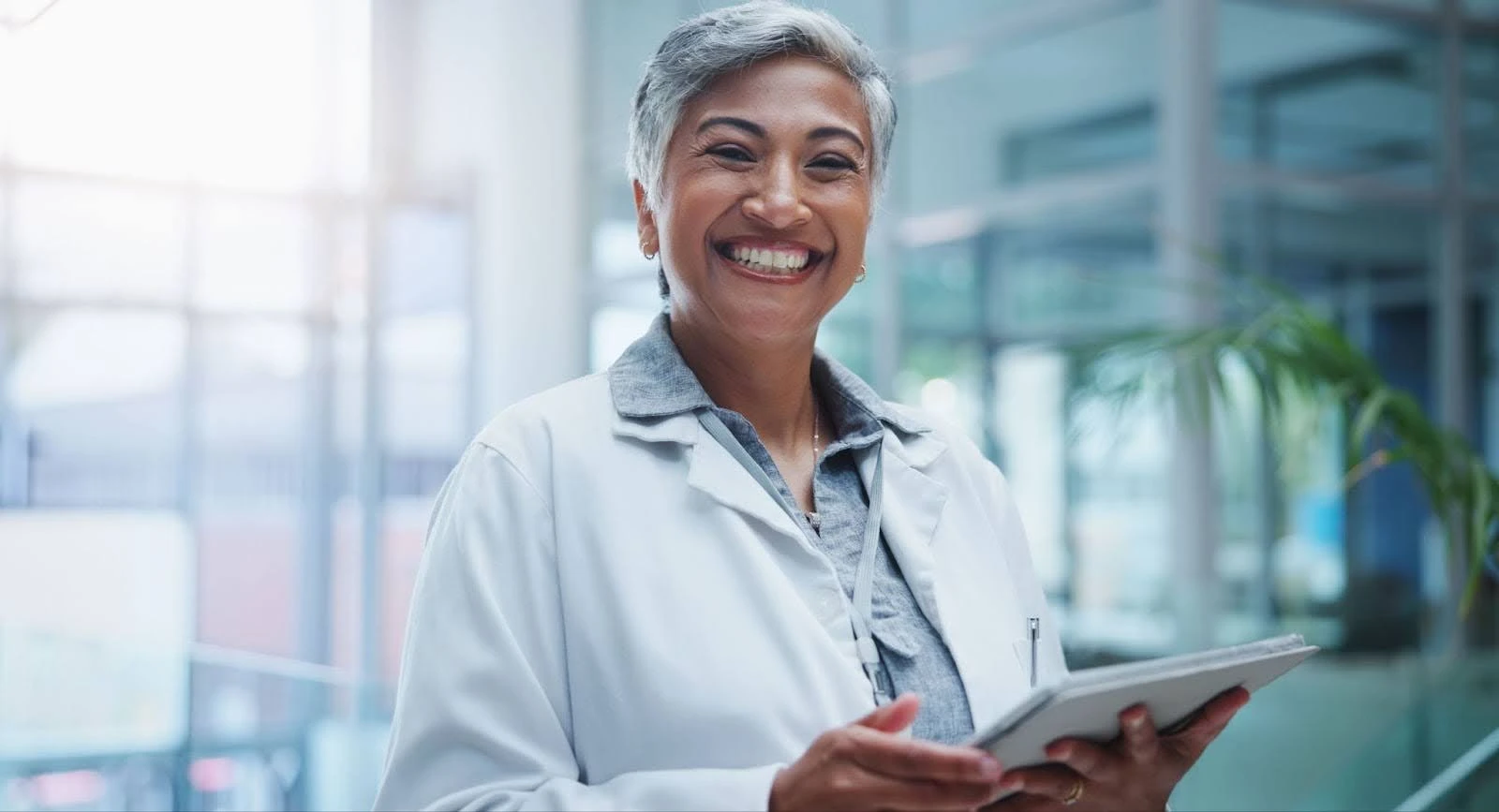 Enfermeira sorridente em ambiente clínico moderno, segurando um tablet e emanando profissionalismo e acolhimento.