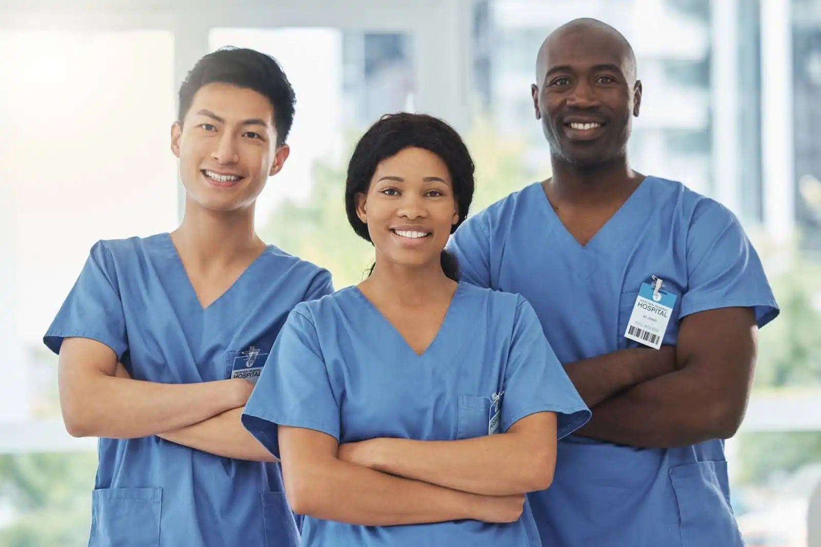 Equipe de profissionais da saúde sorrindo, vestindo uniformes azuis em ambiente hospitalar. Demonstram alegria e união no trabalho em equipe.