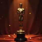 Imagem do famoso prêmio Oscar, uma estatueta dourada em formato humano, simbolizando a excelência no cinema. Destaca-se em um fundo de pano vermelho.