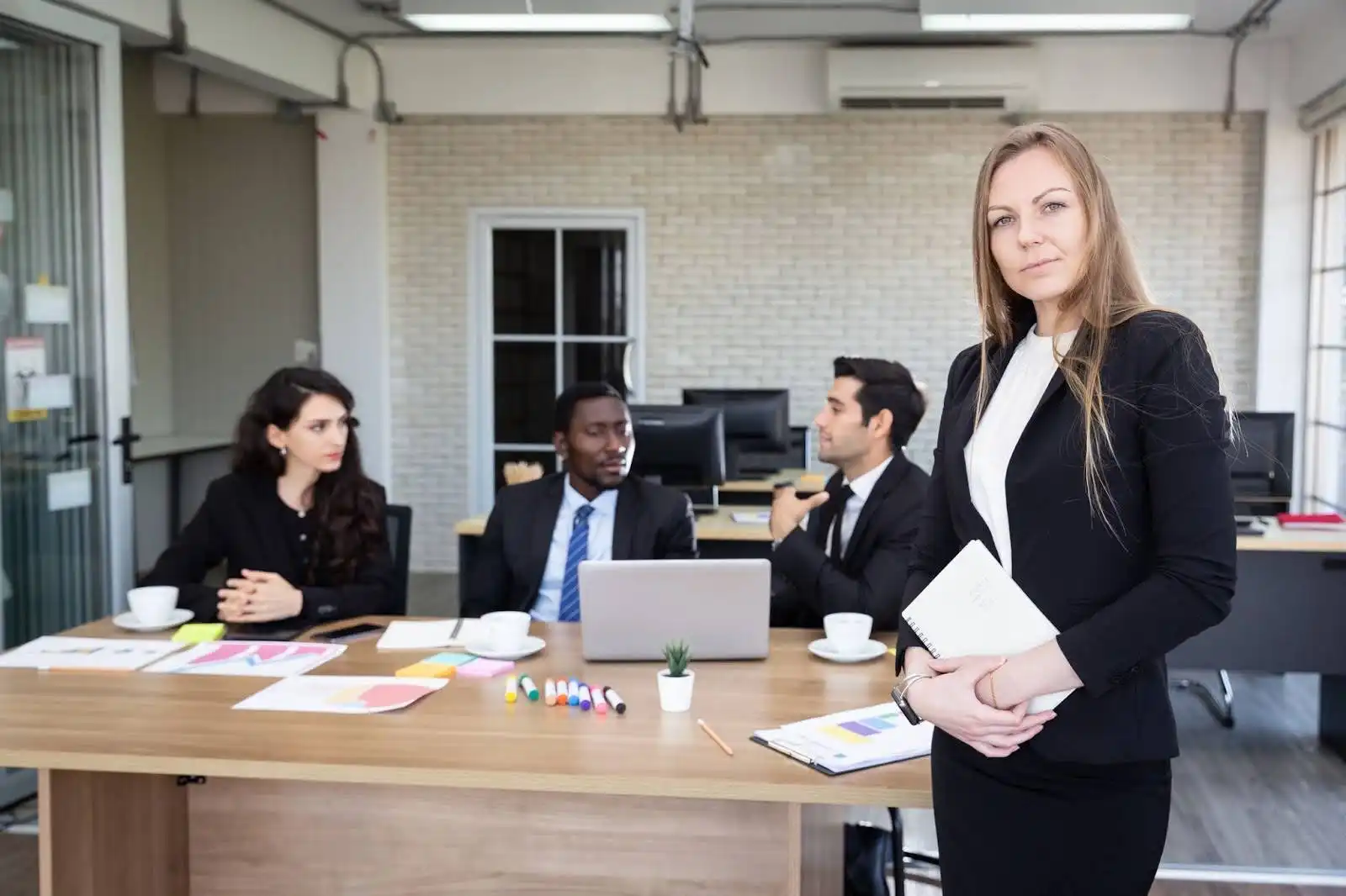 Grupo de profissionais em uma reunião, discutindo estratégias em escritório moderno com mesa de trabalho e equipamentos de tecnologia.