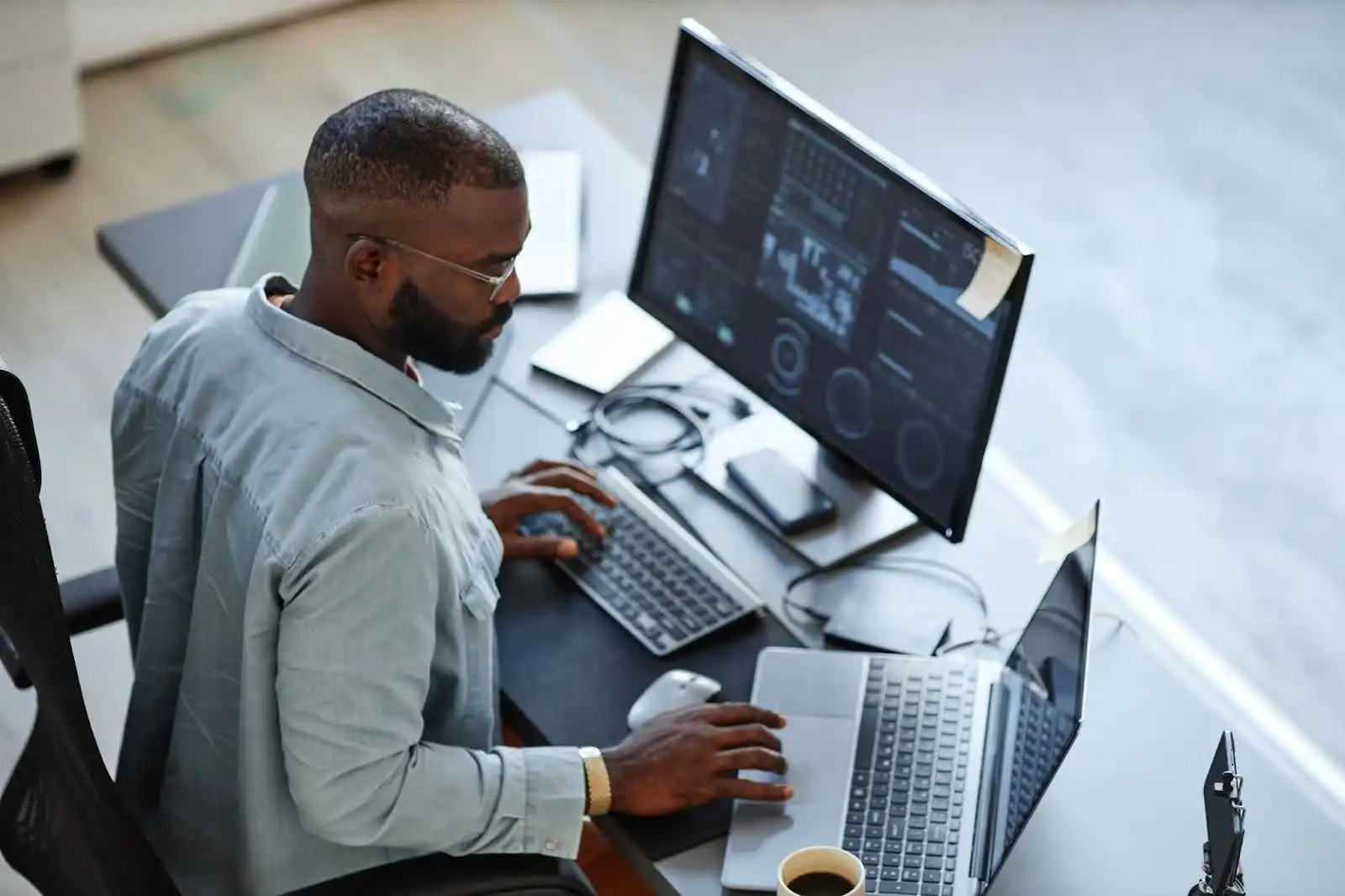 Homem trabalhando em um ambiente moderno com computadores, analisando dados e gráficos em múltiplas telas. O foco é na produtividade e tecnologia.