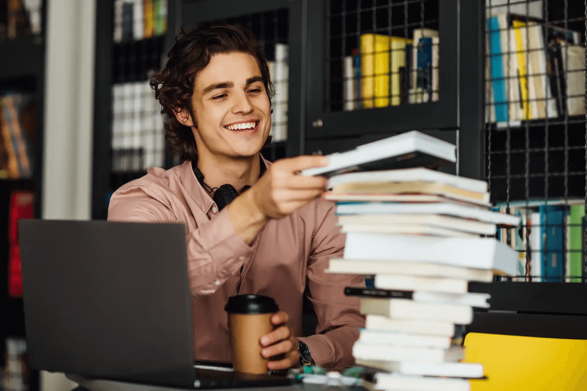 Estudante sorridente organizando livros e anotações para preparação para o ENEM, em ambiente de estudo com laptop e muita dedicação.