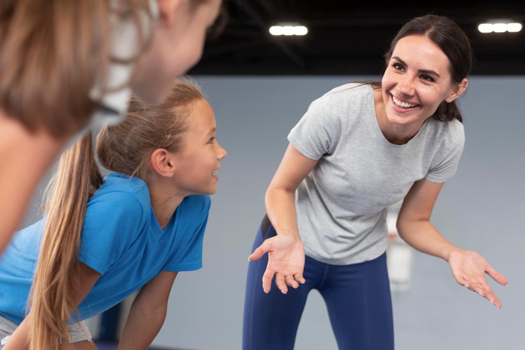 Instrutora de ginástica ensinando duas crianças em uma aula de educação física, promovendo saúde e exercícios físicos para crianças.
