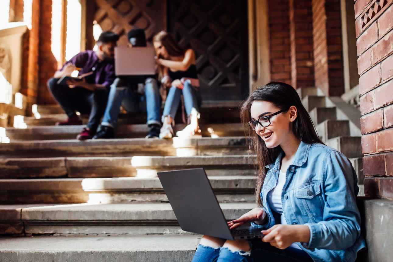 Estudante sorrindo em ambiente acadêmico, usando notebook em escadaria de faculdade, representando possibilidades de ingresso na graduação mesmo para quem não fez o Enem.