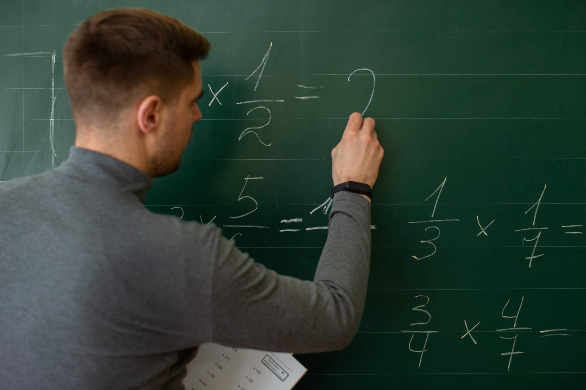 Professor escreve cálculos de matemática no quadro verde, com operações e equações desenhadas a giz, representando a formação pedagógica em matemática para futuros docentes.