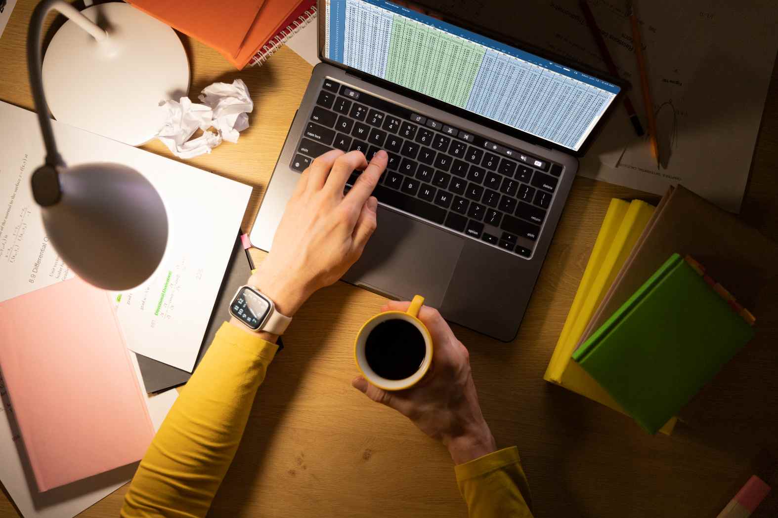 Pessoa organizando os estudos em uma mesa com notebook aberto, materiais, anotações e café, mostrando a rotina de planejamento para manter o EAD mesmo após o trabalho.