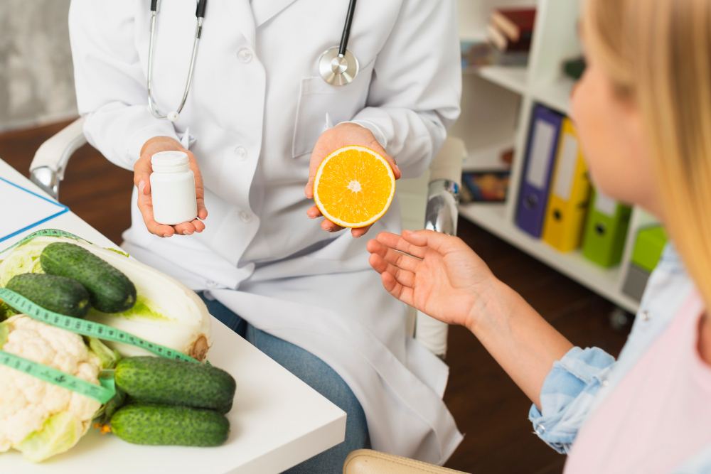 Nutricionista em consultório orienta paciente sobre alimentação saudável, segurando um copo de leite e uma laranja cortada ao meio durante a consulta.