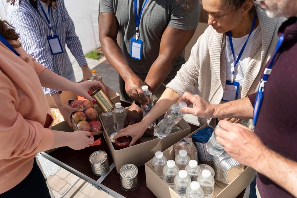 Equipe de voluntários organiza doações em caixas, separando alimentos e bebidas e distribuindo itens como garrafas e conservas em um evento comunitário.